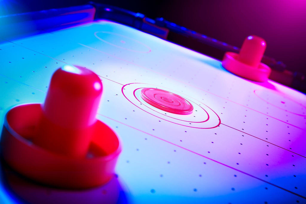Dramatic lit air hockey table with puck and paddles.